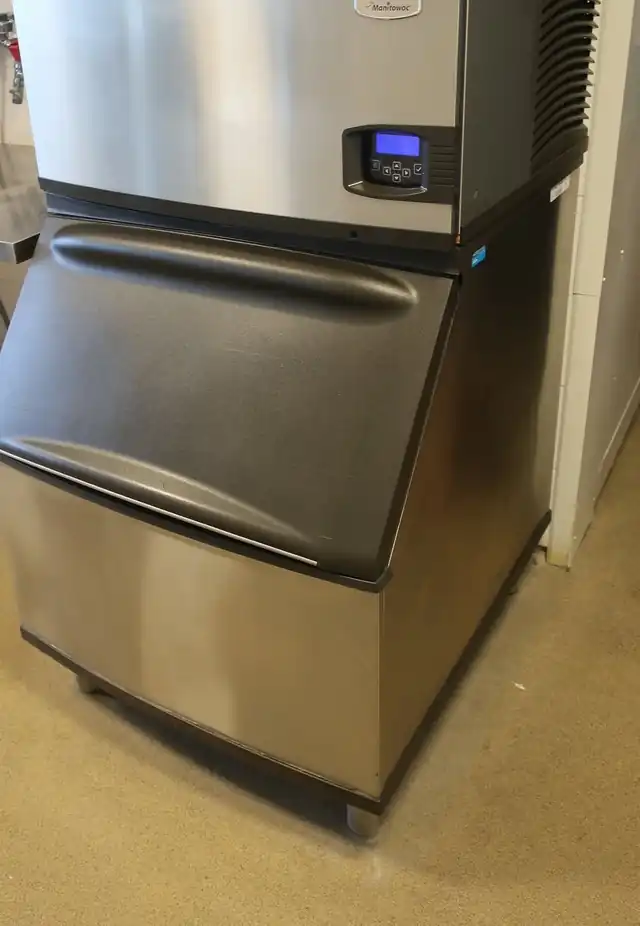 A stainless Manitowoc ice machine on its bin in a commercial kitchen