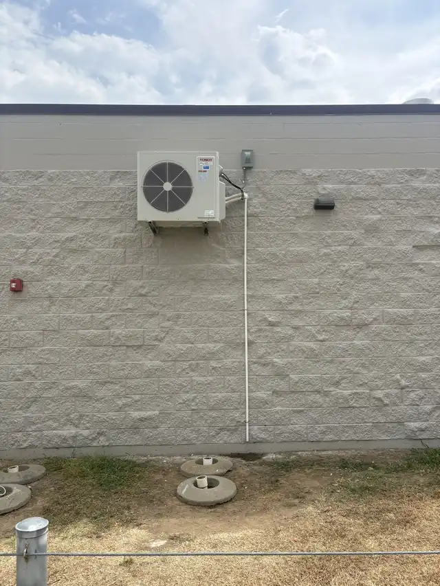 A mini-split outdoor unit mounted high on a block wall under a blue sky