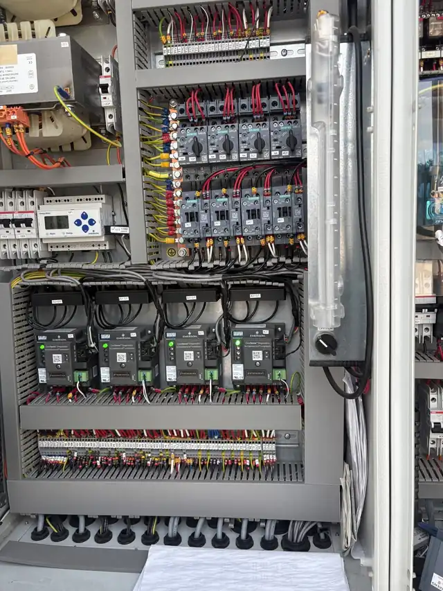 An open commercial refrigeration control cabinet with rows of contactors and compressor controllers