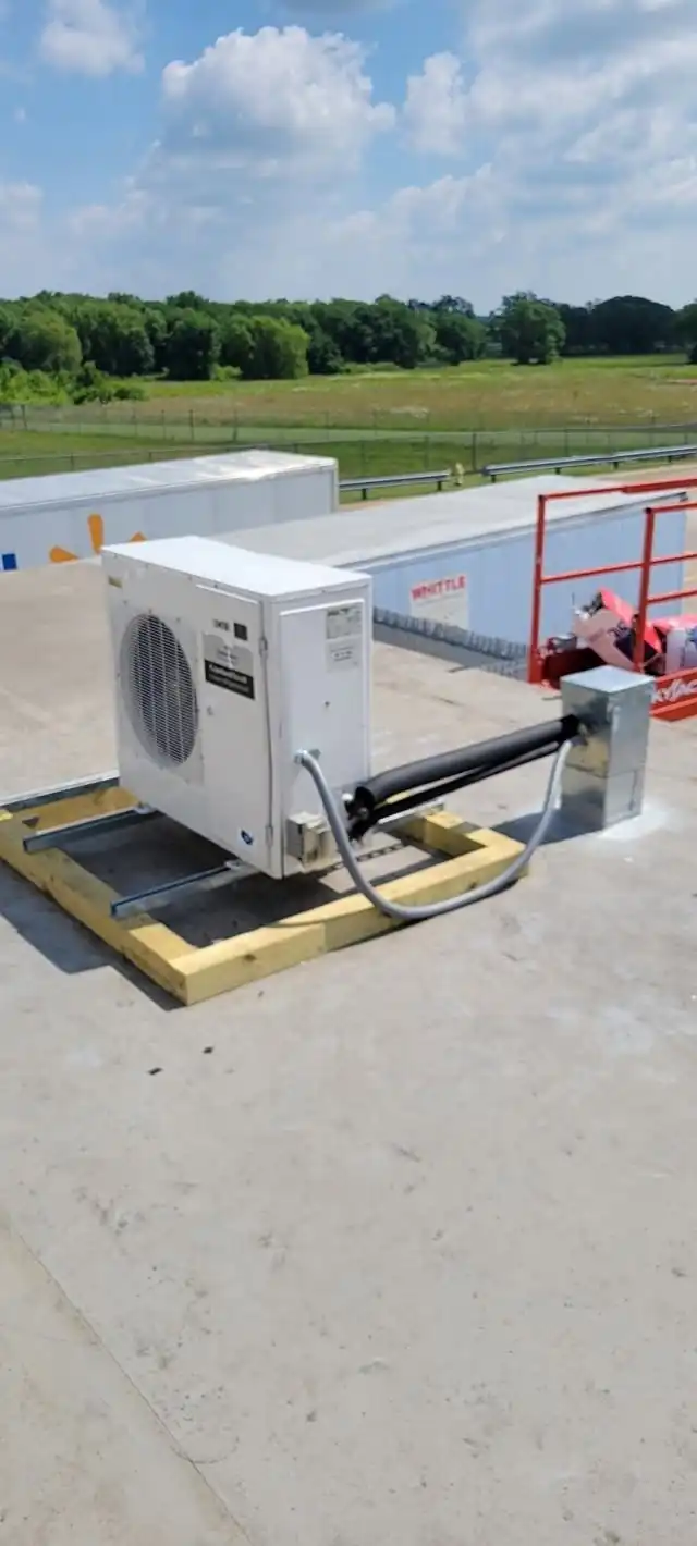 Mini-split outdoor unit on a timber stand on a flat roof, with the line set run along the roof