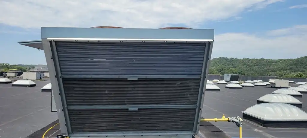 A rooftop unit with a large condenser coil, skylights and hills behind