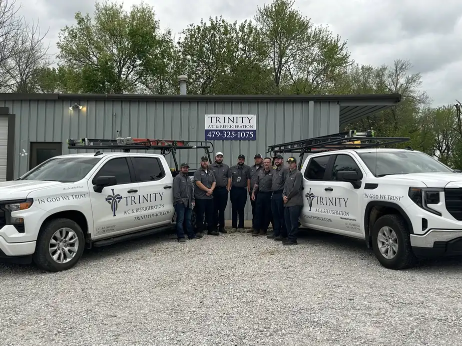 The Trinity crew in matching grey work shirts lined up between two lettered Trinity trucks in front of the shop sign